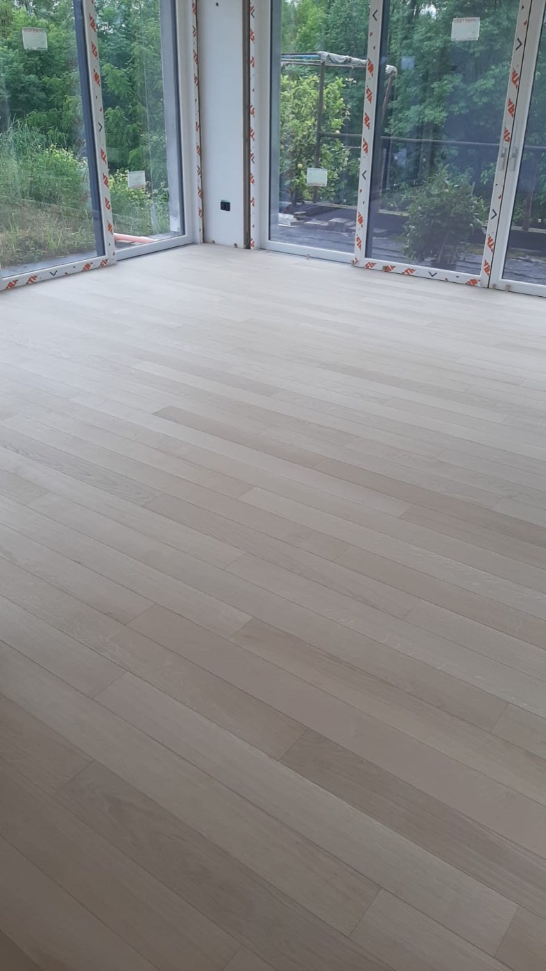Pavimento in rovere chiaro appena posato in un ambiente luminoso con grandi vetrate sul giardino