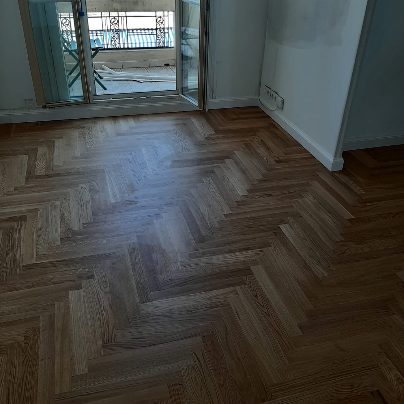 Pavimento a spina di pesce in legno scuro in un ambiente con vista sul balcone